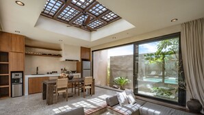 Uma cozinha moderna com armários de madeira, um espaço de refeições com mesa e cadeiras, e uma grande porta de vidro deslizante que dá para um pátio com vista para áreas verdes.