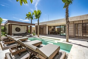 A modern outdoor pool area with lounge chairs, palm trees, and a contemporary building with large windows. - Ukiyo Villa II Pererenan (Canggu)