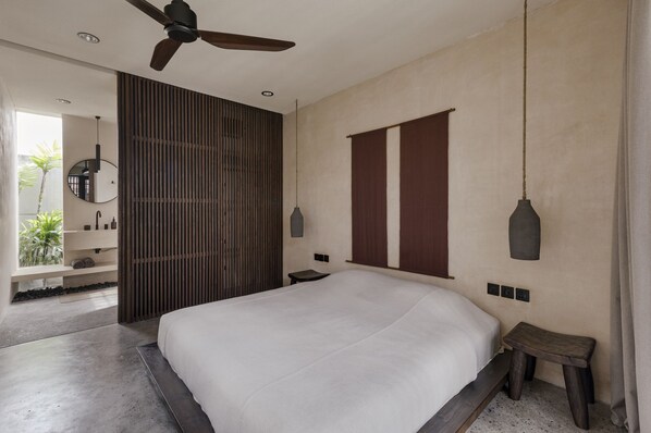 Un dormitorio moderno con una cama grande, un ventilador de techo, una mesita de noche y vistas a un balcón con plantas.
