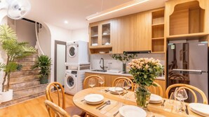 A modern kitchen with wooden cabinets, a built-in washing machine, and a dining area set for four with a vase of flowers.