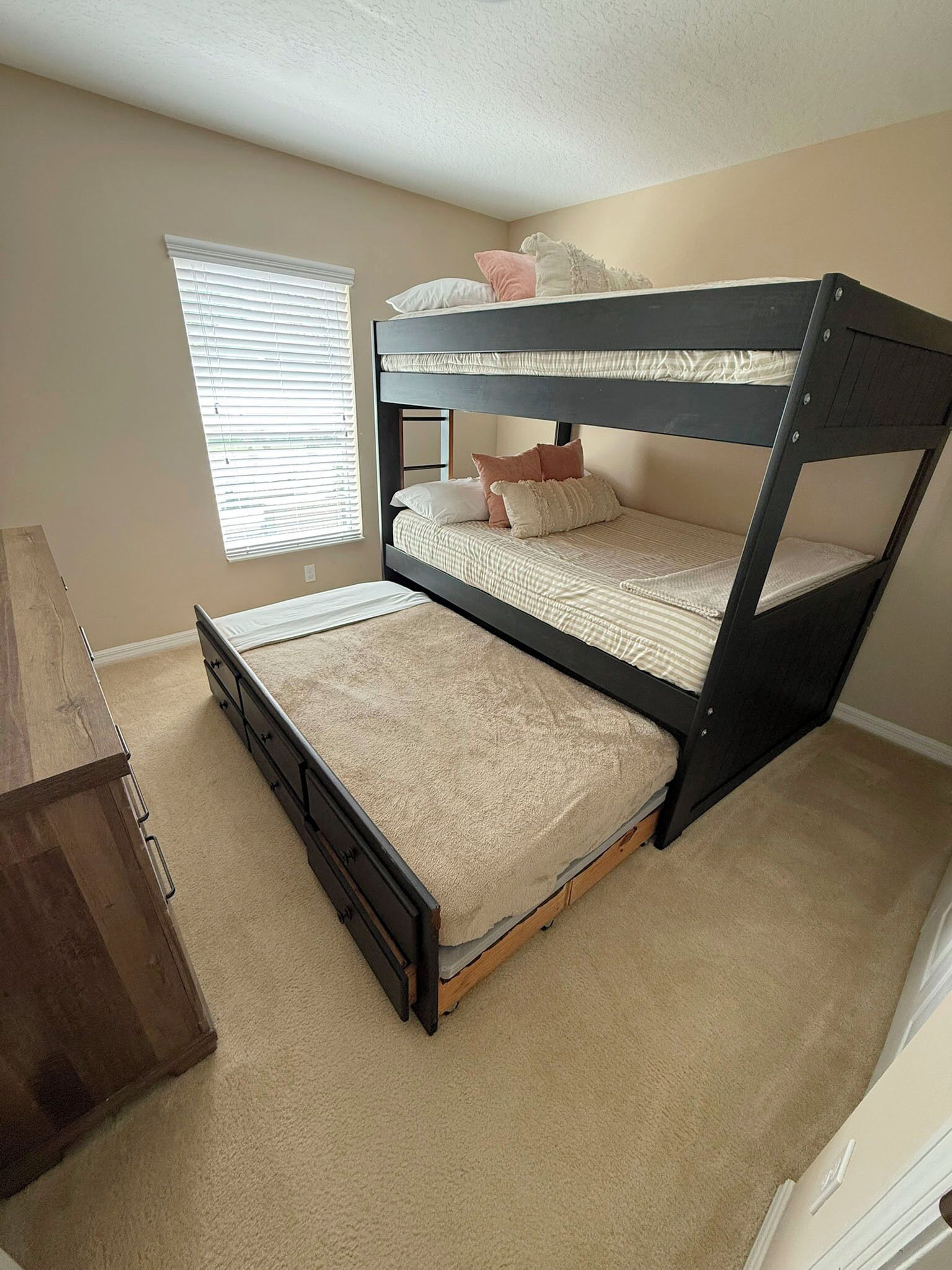 A bunk bed with a wooden frame, a desk, and a window with blinds.