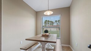 Un espace repas avec une table et des bancs en bois, un luminaire suspendu et une fenêtre équipée de stores.