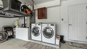 A laundry area with two front-loading washing machines, a drying rack, and a utility cart.