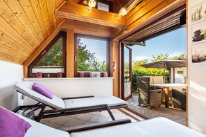 Un solárium con techo inclinado, un asiento junto a la ventana con cojines y una zona de patio con muebles de exterior.