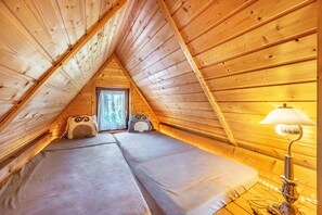 Un dormitorio acogedor en el ático, con paredes de madera, una ventana y una lámpara.