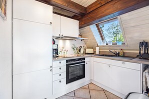 Una cocina con armarios blancos, horno empotrado, ventana con vistas y tragaluz.