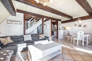 Amplia sala de estar con sofá, mesa de centro y mesa de comedor. Una escalera conduce a un nivel superior.
