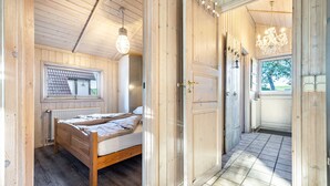 Een houten kamer met een bed, een radiator, een raam en een deur die uitkomt op een balkon.