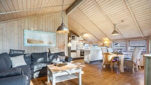 Een gezellig interieur met houten plafond, een bank, een eettafel en een keukenhoek.