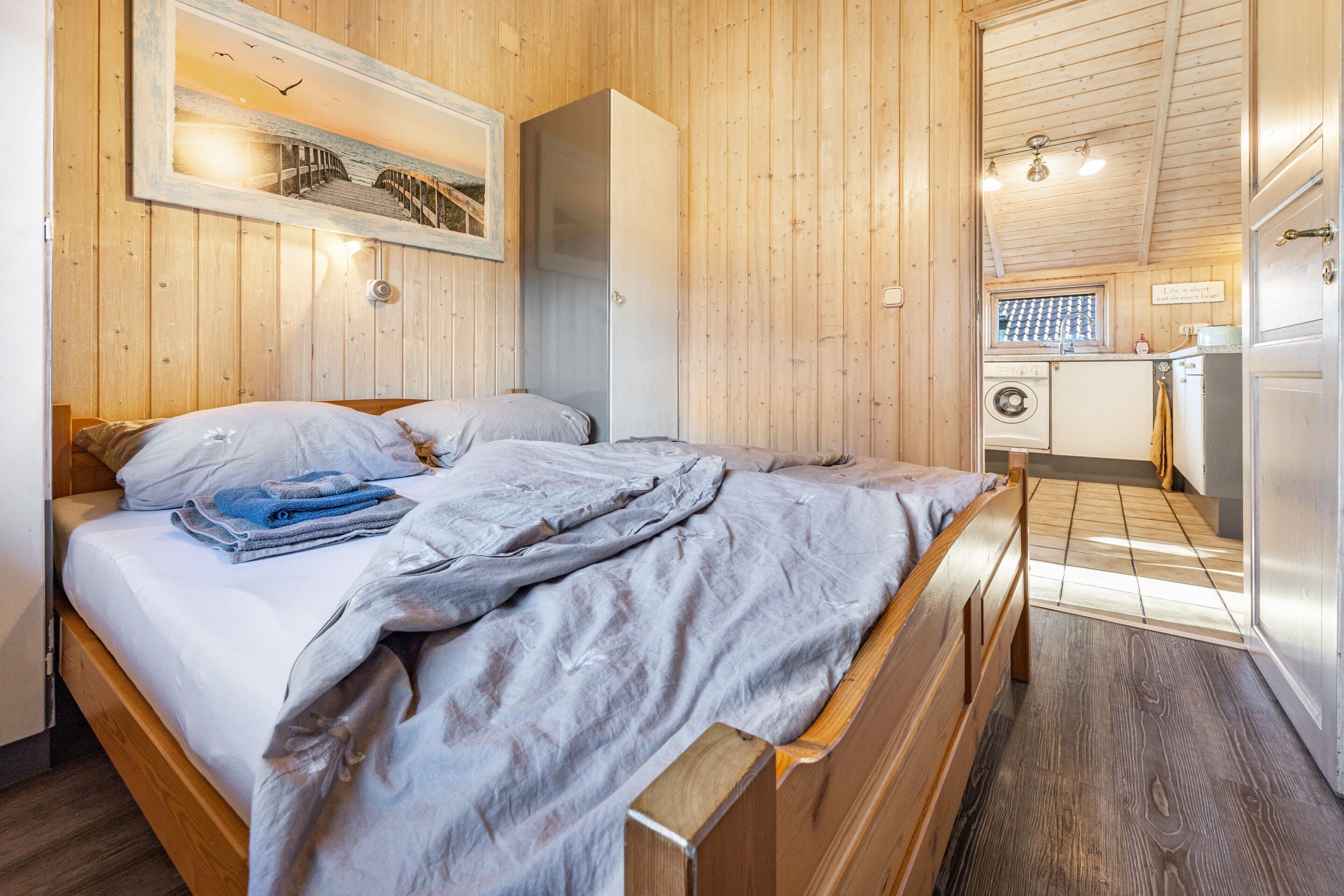 Een kamer met houten lambrisering, een bed, een kledingkast en een keukenhoek.