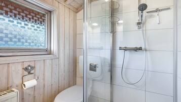 Un baño con inodoro, ducha con cerramiento de vidrio y ventana con diseño de ladrillo.