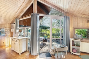 Interior de una cabaña de madera con comedor, una encimera de cocina y vistas al exterior.