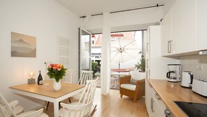 A modern kitchen with white cabinets, a dining area with a wooden table and white chairs, and a view through an open door to an outdoor patio. - Apartment 'Fewo Romeo und Julia' with Private Terrace and Wi-Fi (Bamberg)