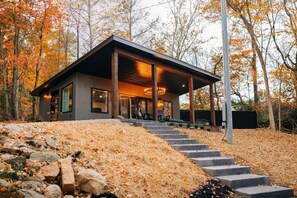 Une maison moderne dotée d’un porche abrité, d’un escalier en pierre et offrant une vue sur les arbres aux couleurs automnales.