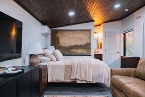 Une chambre à coucher avec un lit, des tables de chevet, une lampe, un tableau et une vue sur l’extérieur.