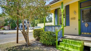 A yellow building with a blue door and green accents, a small porch with steps, and a tree with pink flowers. - Charming 2-bedroom house with WiFi, AC in enchanting downtown Opelousas. (Opelousas)