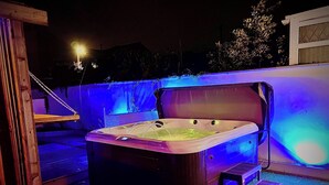 Een kuip met warm water, een houten bank en treden, omgeven door een houten terras en een muur met blauw licht.
