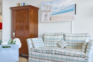 Un salón con sofá escocés, un aparador de madera y un adorno de temática playera.