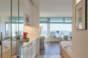 A compact hotel room with a kitchenette, a dining area, and a large window offering a sea view.