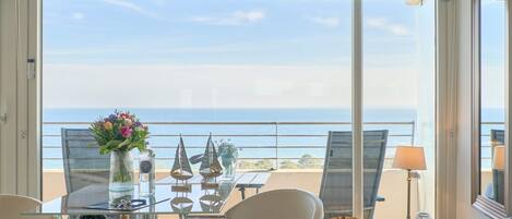 A balcony with a table, chairs, and a view of the sea.