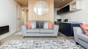 En moderne stue med en grå sofa, et rundt spejl og et køkken i baggrunden.