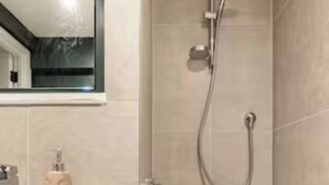 Et moderne badeværelse med badekar, brusebad med håndbruser og vask med sæbedispenser.