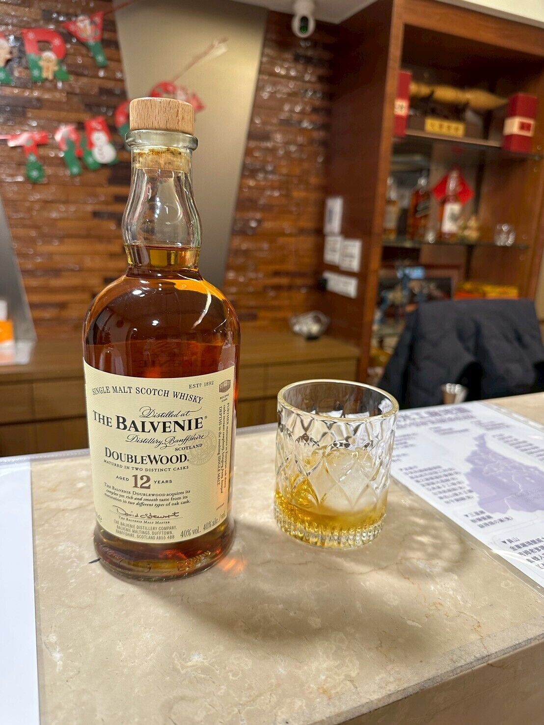 Una botella de whisky The Balvenie Doublewood y un vaso con cubitos de hielo sobre una mesa.