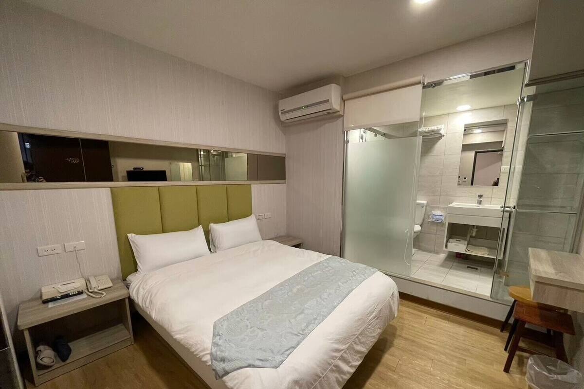 Een hotelkamer met een bed, nachtkastje en een douchecabine met glazen wanden.