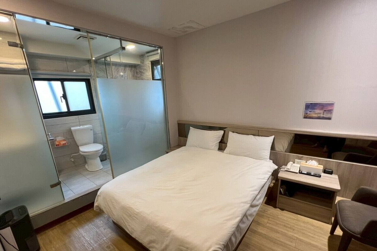 Een hotelkamer met een bed, een bureau met stoel, een toilet en een douche.