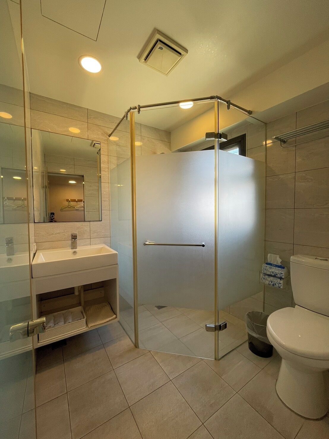 Un baño moderno con ducha de vidrio, lavamanos con espejo y retrete.