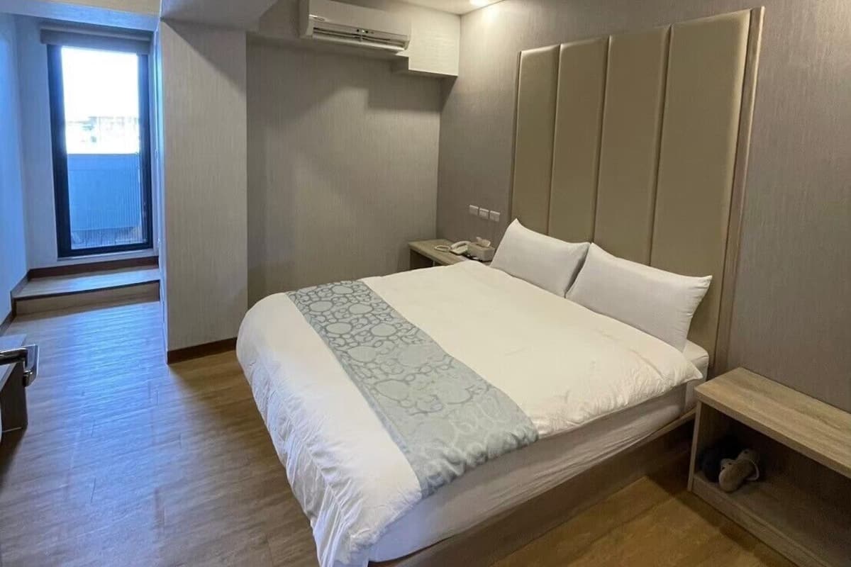 Een moderne slaapkamer met een groot bed, een nachtkastje, een airconditioning en uitzicht op een balkon.