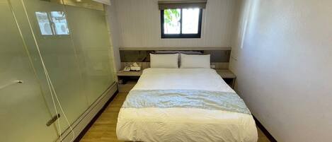 A hotel room with a bed, a nightstand, a window, and a glass door.