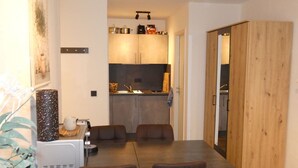 Ein Essbereich mit Tisch und Stühlen, im Hintergrund eine Küche und ein Holzschrank.
