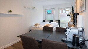 Ein Hotelzimmer mit Bett, Esstisch mit Stühlen, einer Kaffeemaschine und einem Fenster mit Blick auf Gebäude.