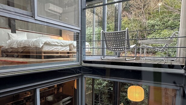 Un intérieur moderne avec un balcon fermé par des baies vitrées, un coin repas doté d’une table ronde et un espace salon confortable agrémenté de coussins.