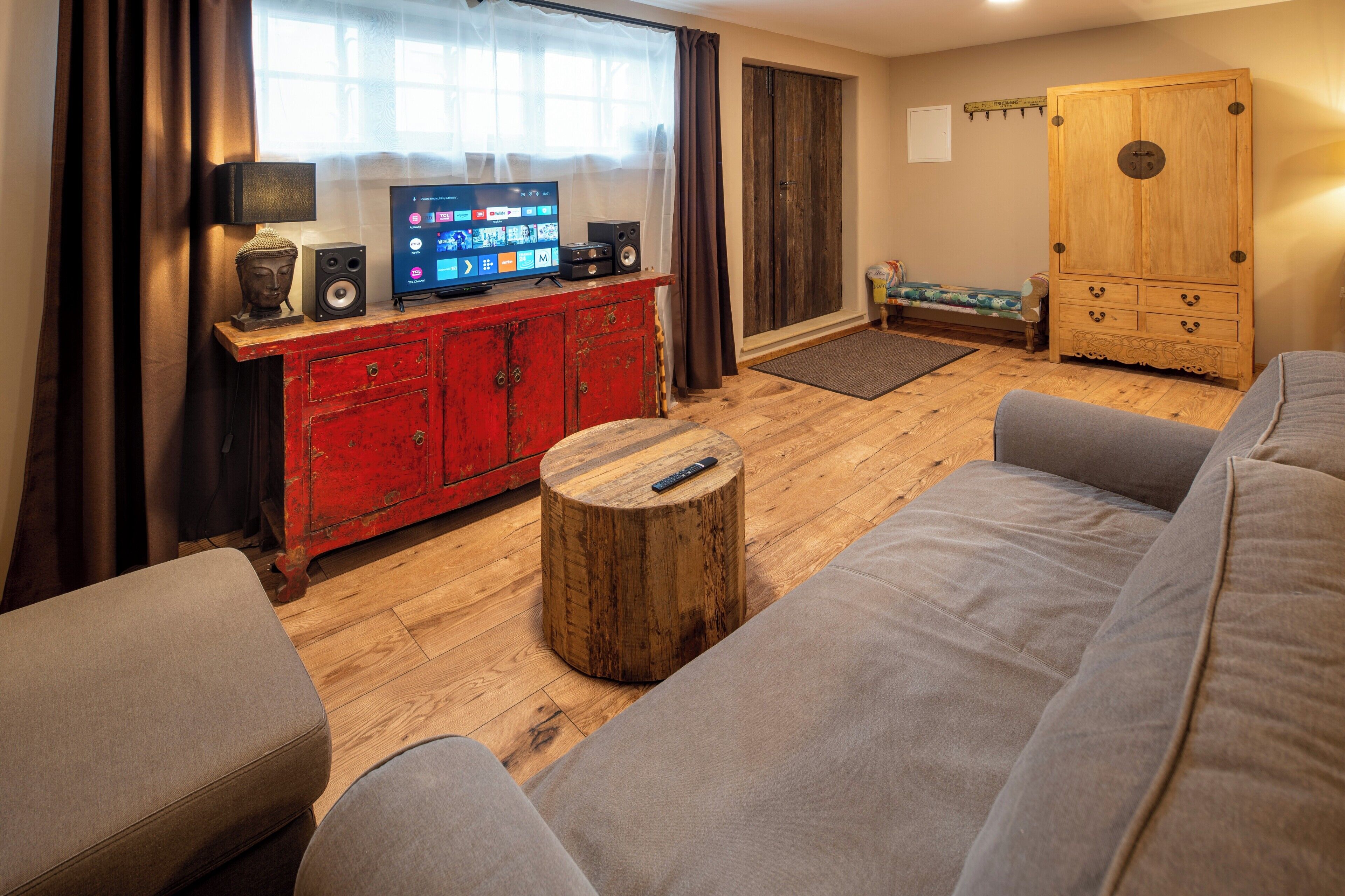 A living room with a red cabinet, a wooden coffee table, a grey sofa, a television, and a wardrobe.