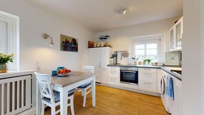 A modern kitchen with white cabinetry, a wooden dining table, and a built-in oven. - Modern apartment with terrace and sea view. - At the dune (Hörnum (Sylt))