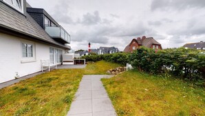 A pathway leading to a white house with a balcony, surrounded by grass and a hedge. - Modern apartment with terrace and sea view. - At the dune (Hörnum (Sylt))