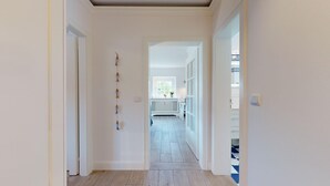 A hallway with a white door on the left, a white radiator, and a window at the end. - Modern apartment with terrace and sea view. - At the dune (Hörnum (Sylt))