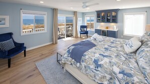A bedroom with a large bed, a chair, a desk, and a view of the ocean. - Ebb's-Oceanfront, Direct Beach Access, Pool, Sleeps 16! (Virginia Beach)