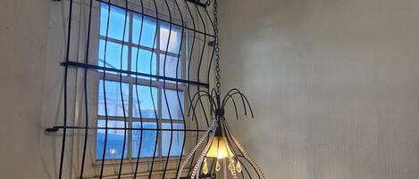 A room with a window covered by a metal grid and a hanging light fixture with a glass shade.