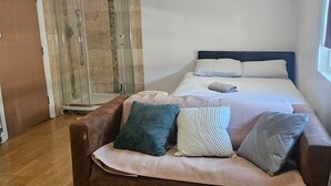 A bedroom with a bed, a shower, and a brown sofa with pillows.