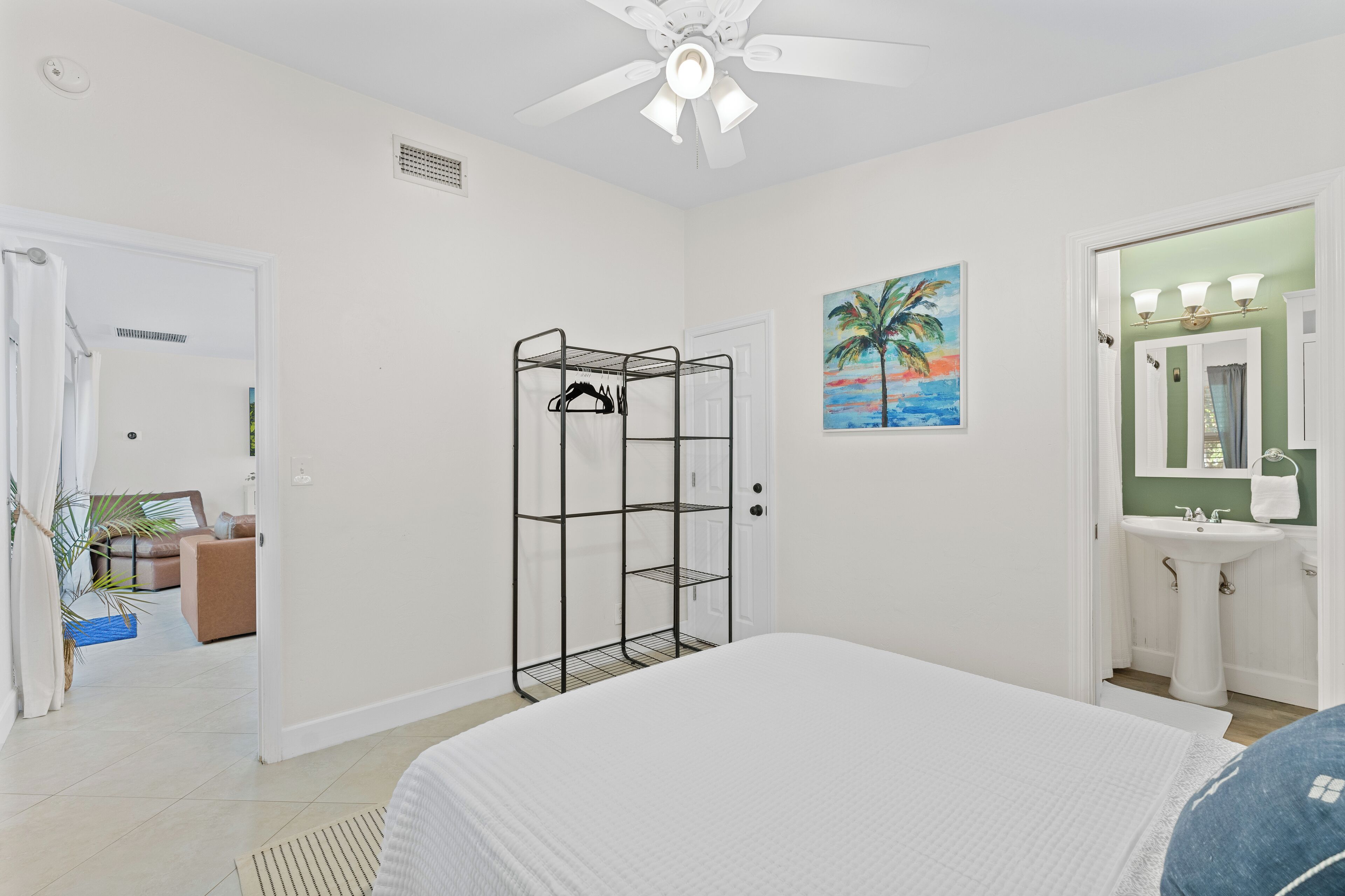 A bedroom with a bed, a wardrobe, a painting, and a bathroom with a sink.