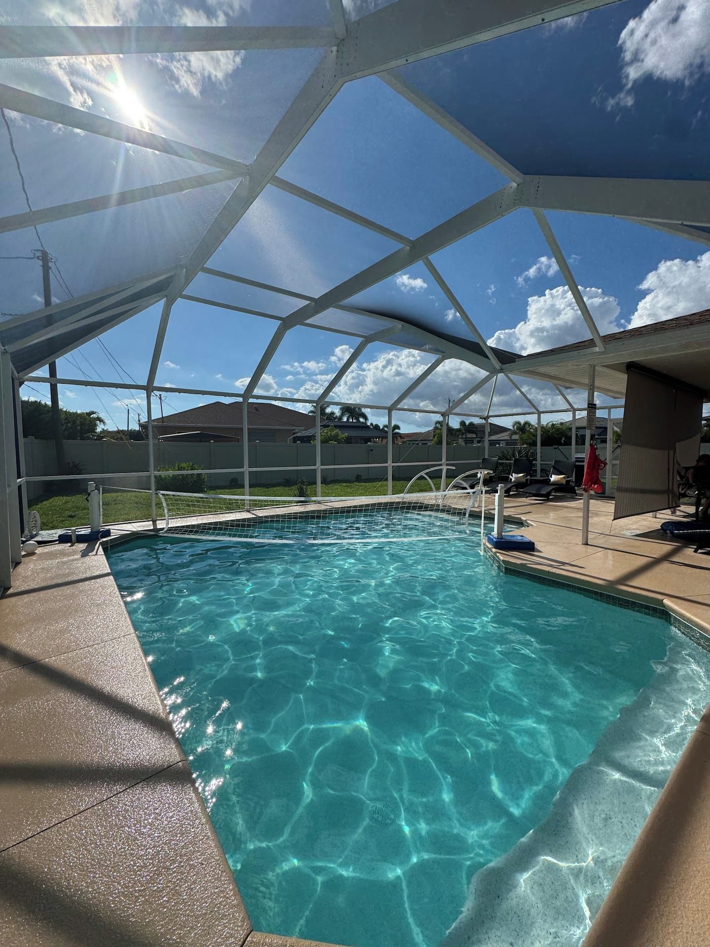 Une piscine d’eau cristalline, d’un bleu éclatant, située sous une pergola blanche, offrant une vue sur le ciel et les environs.
