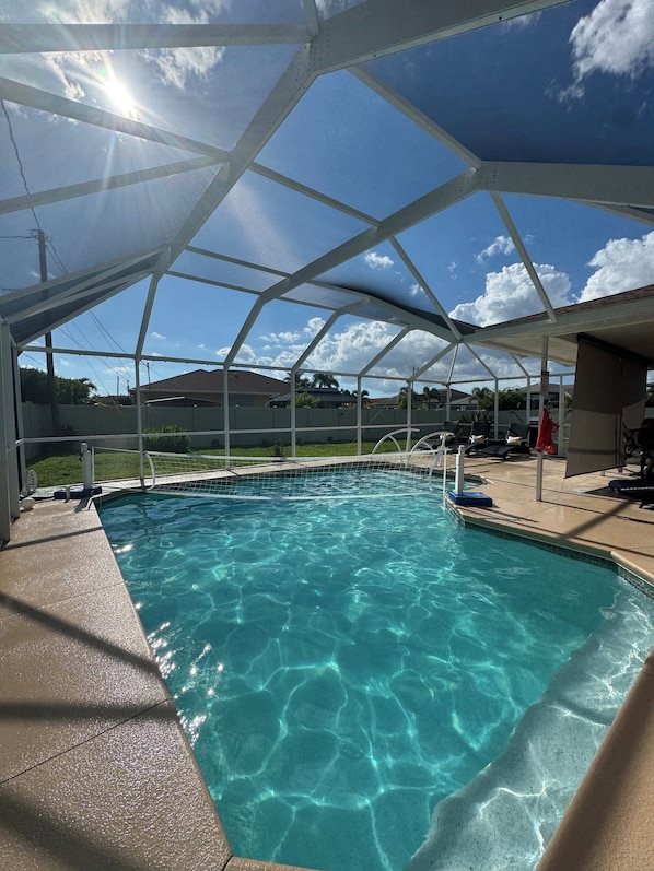 A clear blue pool under a white canopy with a view of the sky and surrounding area.