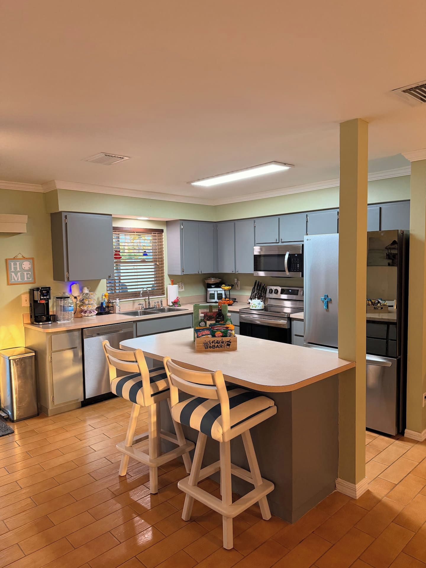 A kitchen with a central island, bar stools, a microwave, an oven, and a refrigerator.