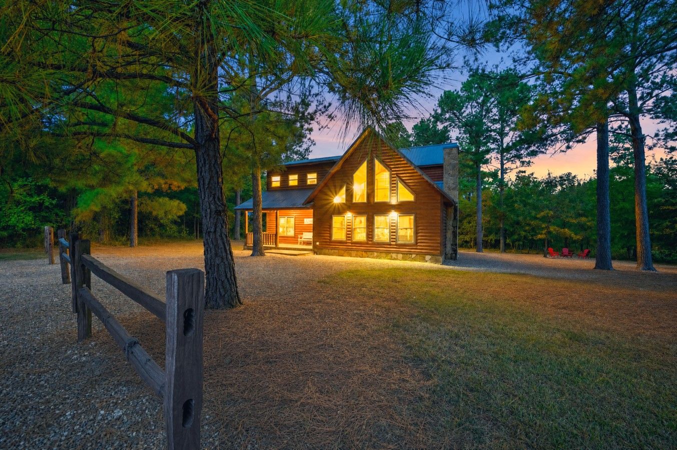 A two-story log cabin with a porch, surrounded by trees.