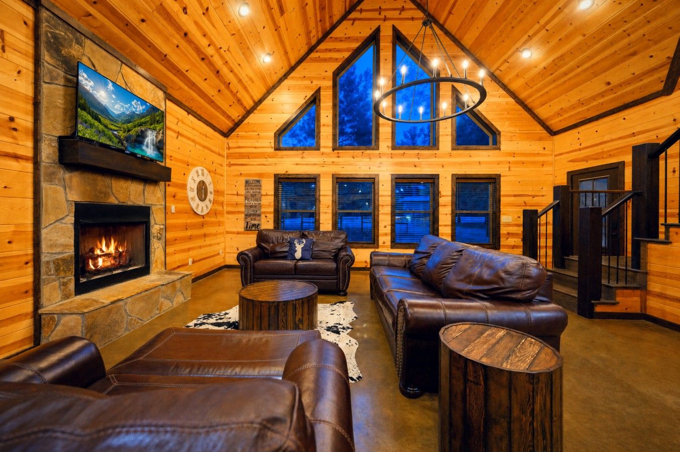 L’intérieur d’une cabane en rondins, avec une cheminée, des canapés en cuir, une table basse ronde et une grande fenêtre donnant sur un paysage montagneux.