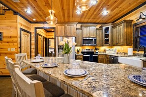 Una cocina con encimeras de granito, armarios de madera, microondas integrado y una zona de comedor con sillas y una mesa dispuesta para dos personas.