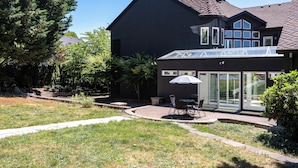 Une maison moderne dotée d’un grand patio, d’une véranda fermée par des baies vitrées et d’une pelouse bien entretenue.